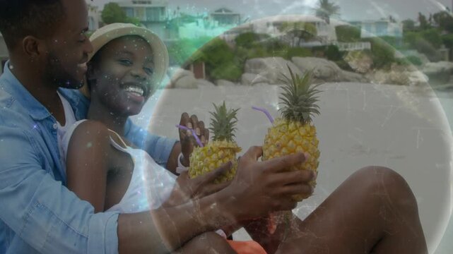 Couple on sand lifting pineapples to camera, sparking glowing globe overlay over scene for travel