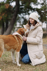 Dog and woman share a gentle moment in a pale winter coat, kneeling on grass as they connect in a park setting, showcasing companionship, care, calm outdoor bonding, warm textures, and mindful