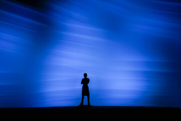 Fototapeta premium Silhouette of a person standing alone against a powerful blue light