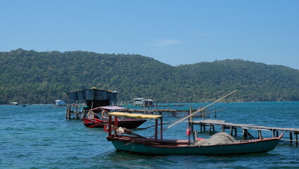 Fototapeta premium traditional fishing boats anchored in a tranquil sea, lush green mountains rise in the distance under a clear sky.