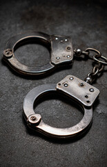 Metal handcuffs with a matte finish and chain links on a dark textured surface, close-animated movie shot emphasizing the metallic texture and locking mechanism
