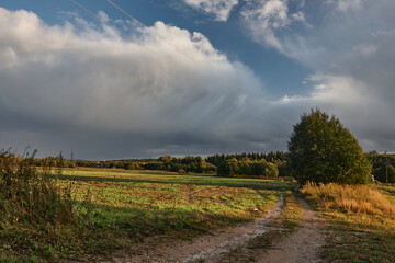 Rural dirt road and field under dramatic cloudy sky