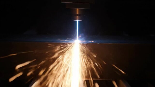Laser cutting metal with sparks and blue laser beam in dark industrial setting. Industry, metalwork, cutting.