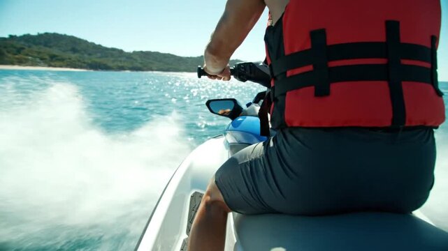 Person in a red life vest riding a jet ski on blue ocean water with a green island in the background on a sunny day.