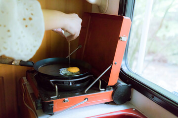 Cooking fried eggs in a frying pan inside a camper van kitchen. Morning breakfast preparation during a vanlife road trip in the forest.