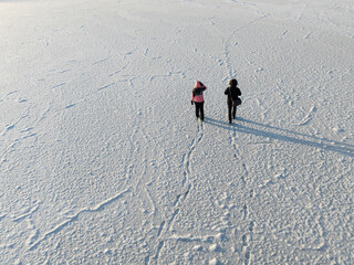 High angle aerial view of two people walking on a vast frozen lake covered in white snow and ice textures