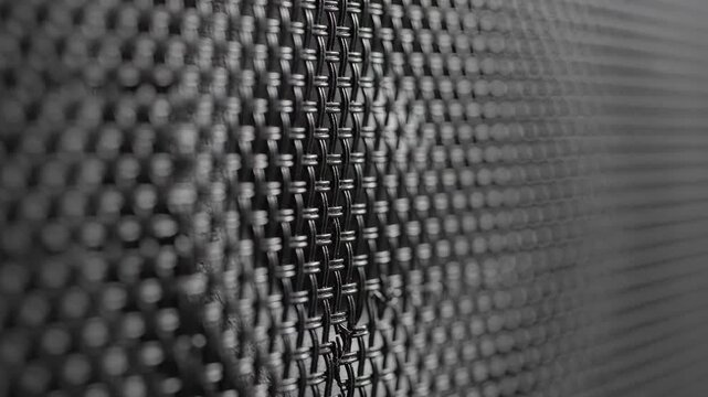Macro close-up of black metal mesh texture. Abstract speaker grille or microphone surface with shallow depth of field. Industrial background pattern
