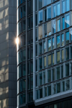Modern glass skyscraper facade in Frankfurt Germany catches sunlight and produces strong reflection over an urban office district skyline