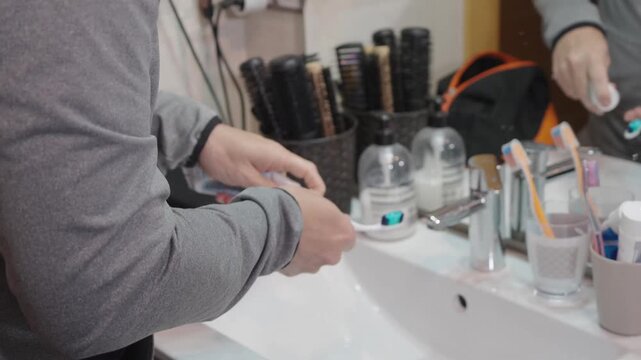 Person squeezing toothpaste onto a toothbrush over the sink during a daily hygiene routine, promoting oral care, dental health, and overall wellness in the bathroom