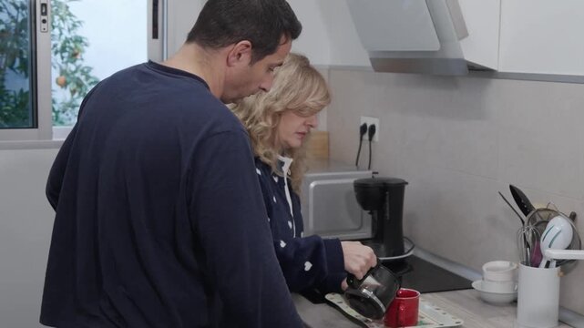 Sleepy woman spilling coffee while her husband watches with concern during their chaotic morning routine in the kitchen, a domestic life concept of human error