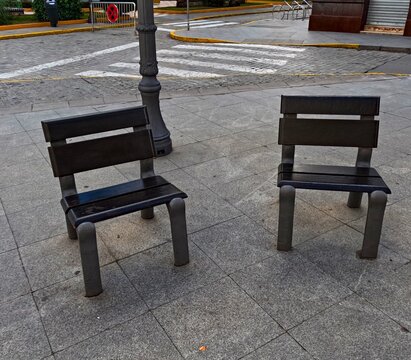 Two empty public benches placed in a quiet urban square in Dos Hermanas, Seville, Spain, symbolizing waiting, pause, separation and everyday life in a traditional Andalusian town