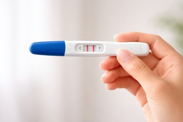 Obraz premium Hand holding pregnancy test showing positive result with two indicator lines on light background.