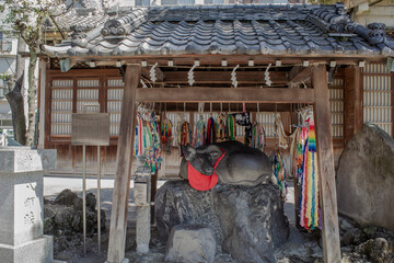 Naklejka premium A calm scene of a stone cow statue, an object of faith, resting quietly in the shrine grounds.