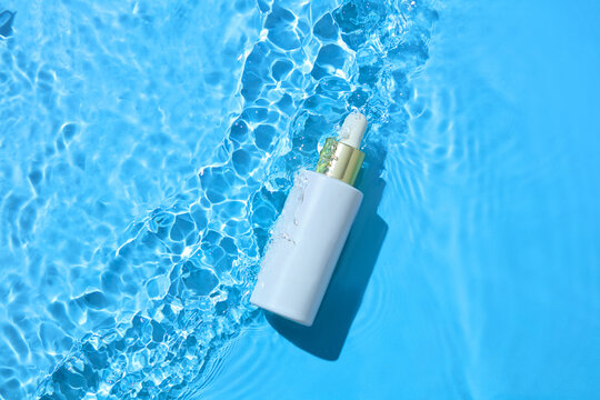 Small pump bottle floating on clear water with light reflections. Bright, modern scene designed for cosmetic promotion and clean branding layouts