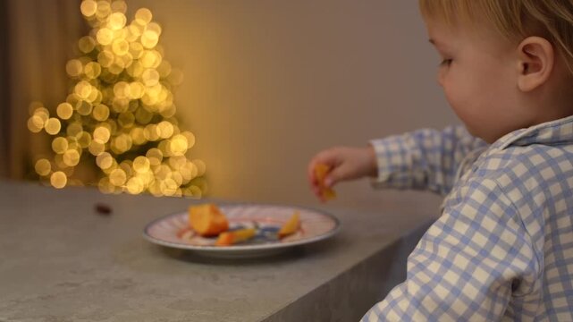 toddler taking a piece of fruit from a plate on the table and eating it.