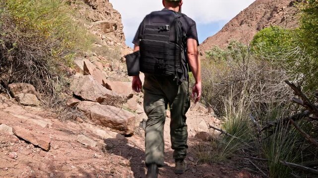 Determined man walks along rocky hiking trail in arid mountainous terrain. Rugged outdoor setting captures adventurous spirit during daytime.