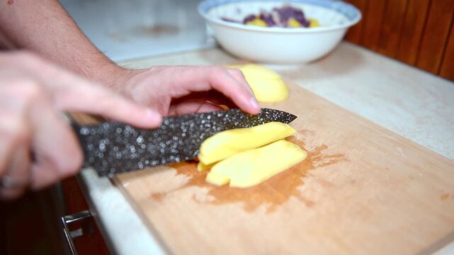 A close-up view of manual potato slicing. The blade glides effortlessly, transforming a whole peeled potato into a pile of ready-to-cook pieces. This simple, meditative process highlights the basics o