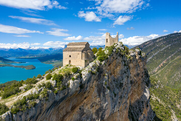 Fototapeta premium Historic stone castle and church rise above a steep rocky escarpment overlooking the brilliant turquoise waters of Mediano lake in Aragon, Spain. Crisp sunlight highlights the rugged limestone