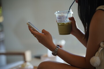 Title: Young woman using a smartphone and holding a cold beverage in a cafe or office.