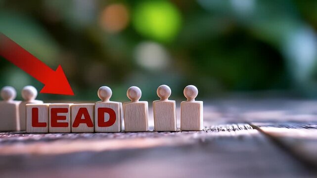 Wooden blocks with the word "LEAD" and miniature people figures, with a downward-pointing red arrow