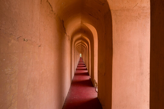 A narrow passageway with repeating arches and textured ochre walls stretches into the distance at Imambara Bara in Lucknow. Soft natural light highlights the red carpet and architectural symmetry