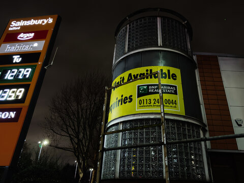 Nighttime city signs and vacant unit BNP Paribas real estate banner in Manchester UK shopping district at dusk