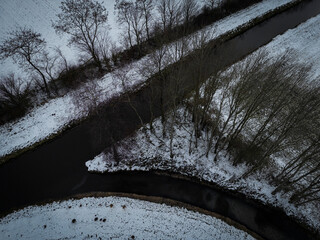 Snowy landscape with trees along a tranquil river in a wintery atmosphere, aerial photograph of a...