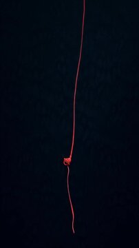 A thin, bright red string hangs suspended against a dark, textured background, with a knot