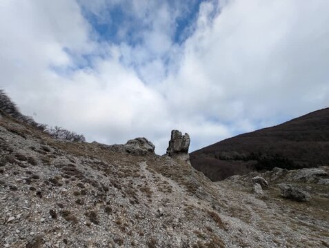 Paesaggio montano arido, con pendii rocciosi e vegetazione secca, sotto un cielo azzurro con nuvole sparse
