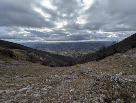 Panorama mozzafiato su una valle montana dall&rsquo;alto di un crinale, con alberi spogli e pendii rocciosi sotto un cielo nuvoloso
