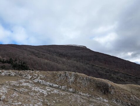 Paesaggio montano invernale, alberi senza foglie e rocce a vista sotto un cielo azzurro con nuvole bianche