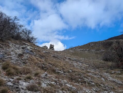 Paesaggio montano arido, con pendii rocciosi e vegetazione secca, sotto un cielo azzurro con nuvole sparse