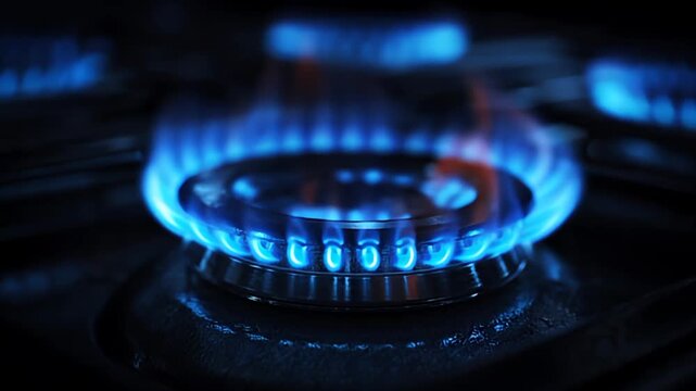 A close-up view of a gas stove burner with blue flames burning intensely on a kitchen stove at night in a dark environment