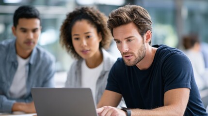 Fototapeta premium Group of three young adults collaborating on a laptop in a modern workspace, engaged in discussion with a bright and open atmosphere enhancing productivity