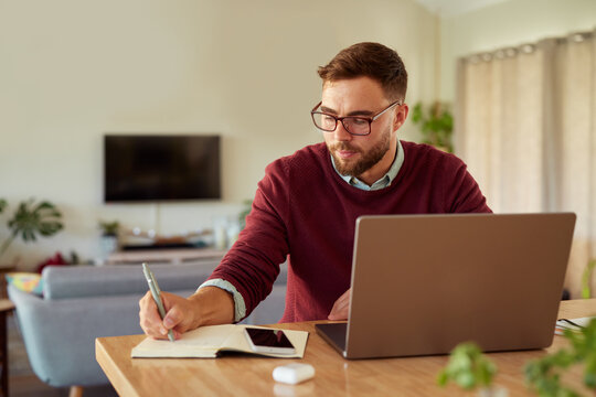 Mid adult casual man writing notes while working at home