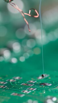 Extreme close-up of a soldering iron tip with a molten solder ball, on a green circuit board