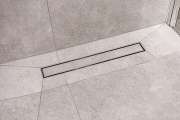 Fototapeta premium Close-up of a sleek linear drain integrated into a light gray stone-tiled shower floor. Clean, geometric lines emphasize modern bathroom design