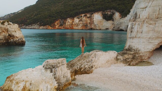 Woman with long hair explores hidden cove and emerald sea cliffs in Kefalonia Greece.