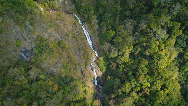 Tall segmented waterfall cascading down rocky cliff face in evergreen forest of Costa Rica.