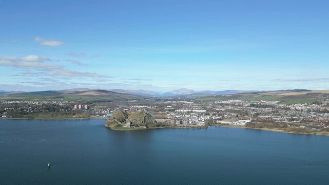Breathtaking aerial tracking shot of the historic Dumbarton Castle perched on a volcanic plug overlooking the River Clyde and the surrounding Scottish landscape.