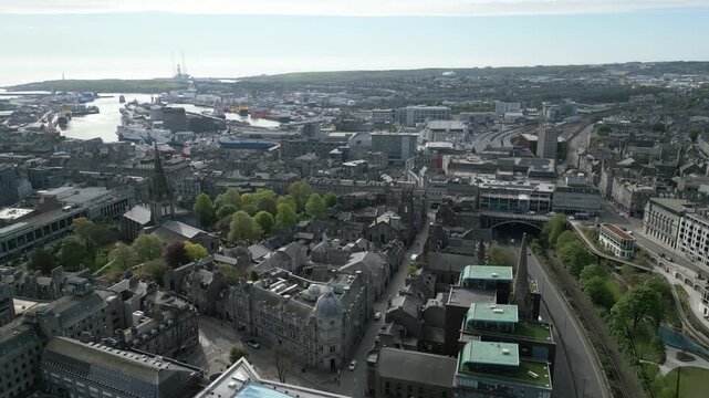 Wide aerial tracking shot over the historic granite architecture of Aberdeen city centre featuring the harbor and urban landscape of Scotland.