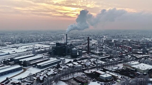 Aerial pull back from snow-covered industrial elevator tower at sunrise with warm golden light over Jelgava cityscape in winter Latvia
