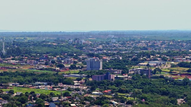 Ascending drone shot above Foz do Igua&ccedil;u showing dense cityscape and distant skyline of Ciudad del Este under clear daylight