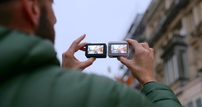 Person holding two action cameras simultaneously comparing their displays on a city street