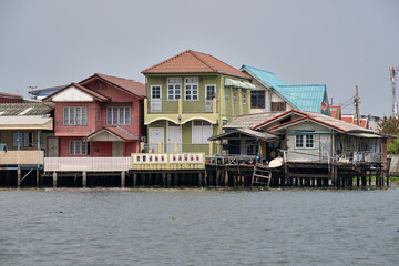 Obraz premium Colorful stilt houses along a waterfront in Bangkok with walkways and a small boat.
