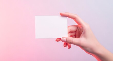 Obraz premium A female hand holding a horizontal blank white card mockup against a soft pastel pink background, ideal for feminine branding or social media promotions.