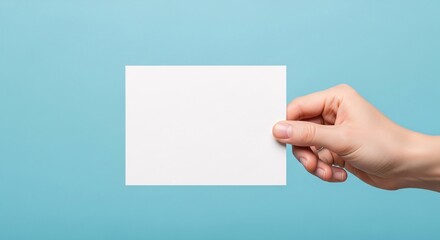 Fototapeta premium A hand holding a horizontal blank white card mockup against a bright, clean sky blue background, creating a fresh and professional look for business identity.