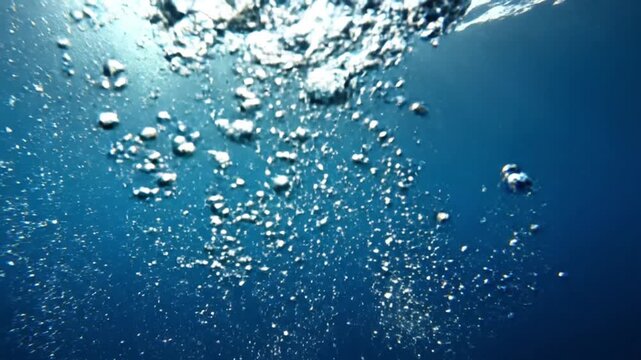 Underwater bubbles rising to the surface in clear blue water with sunlight.