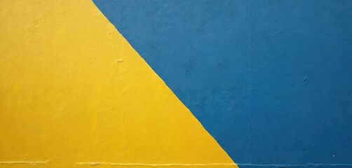 Abstract textured wall divided diagonally yellow lower half blue upper half. Textured cement surface with paint creating graphic art pattern. Bold color block design for backgrounds.