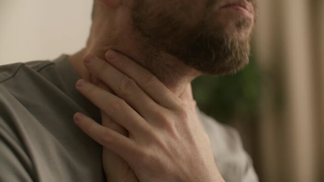 Close up view of man holding his neck with both hands while experiencing sore throat and pain during illness at home